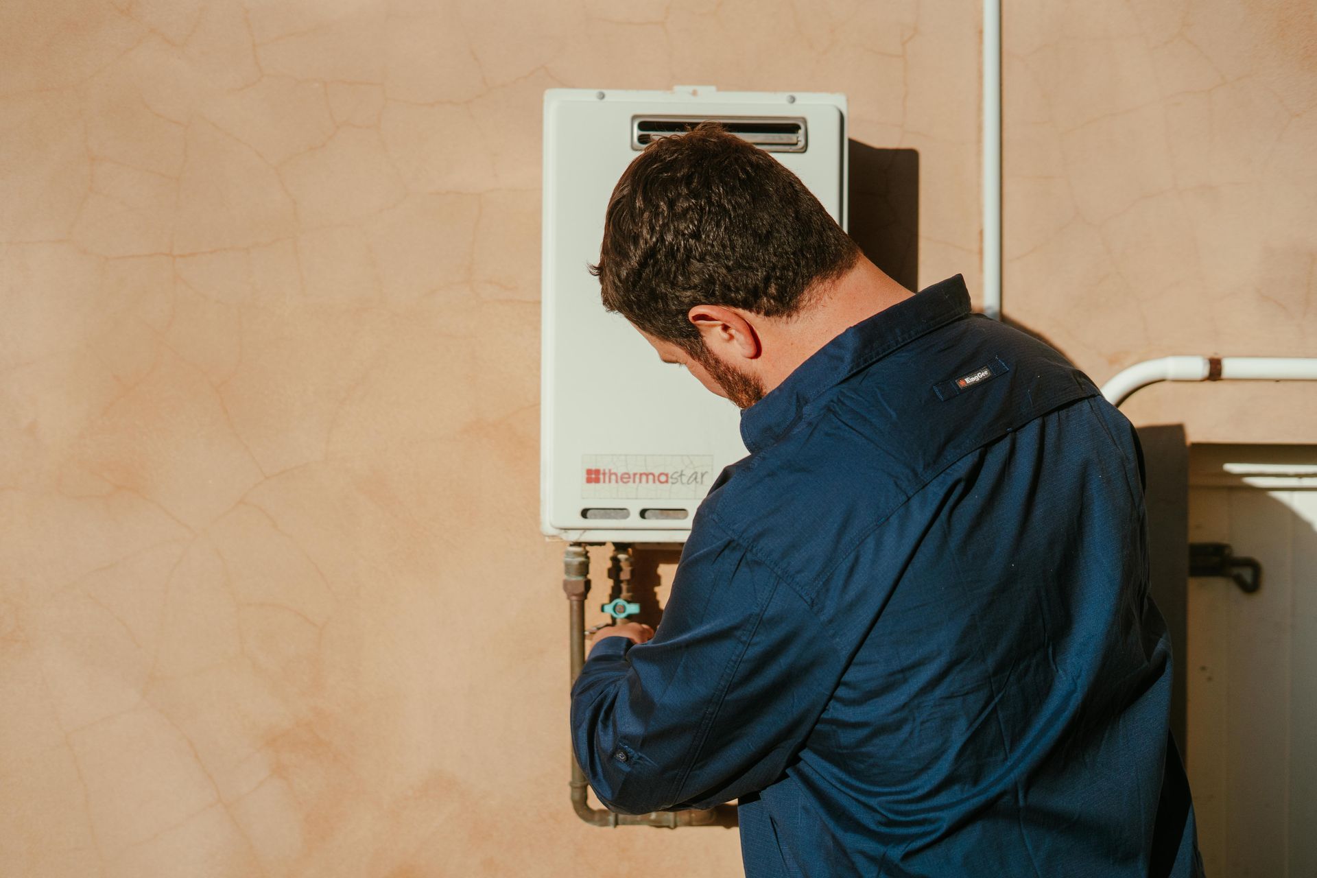Technician inspecting a wall-mounted boiler, facing away in a blue shirt — The Plumbing & Drainage Co. in Bowral, NSW