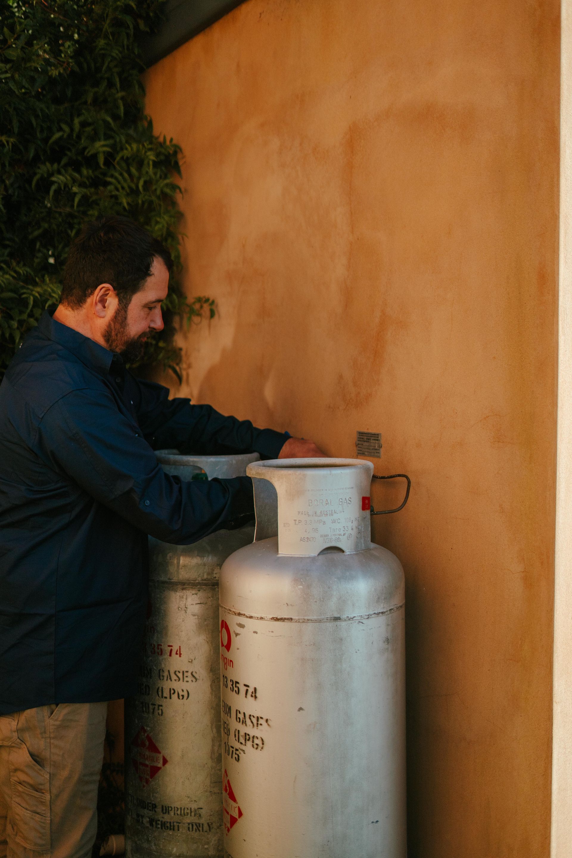Man filling a propane tank beside an orange wall outdoors — The Plumbing & Drainage Co. in Shellharbour, NSW