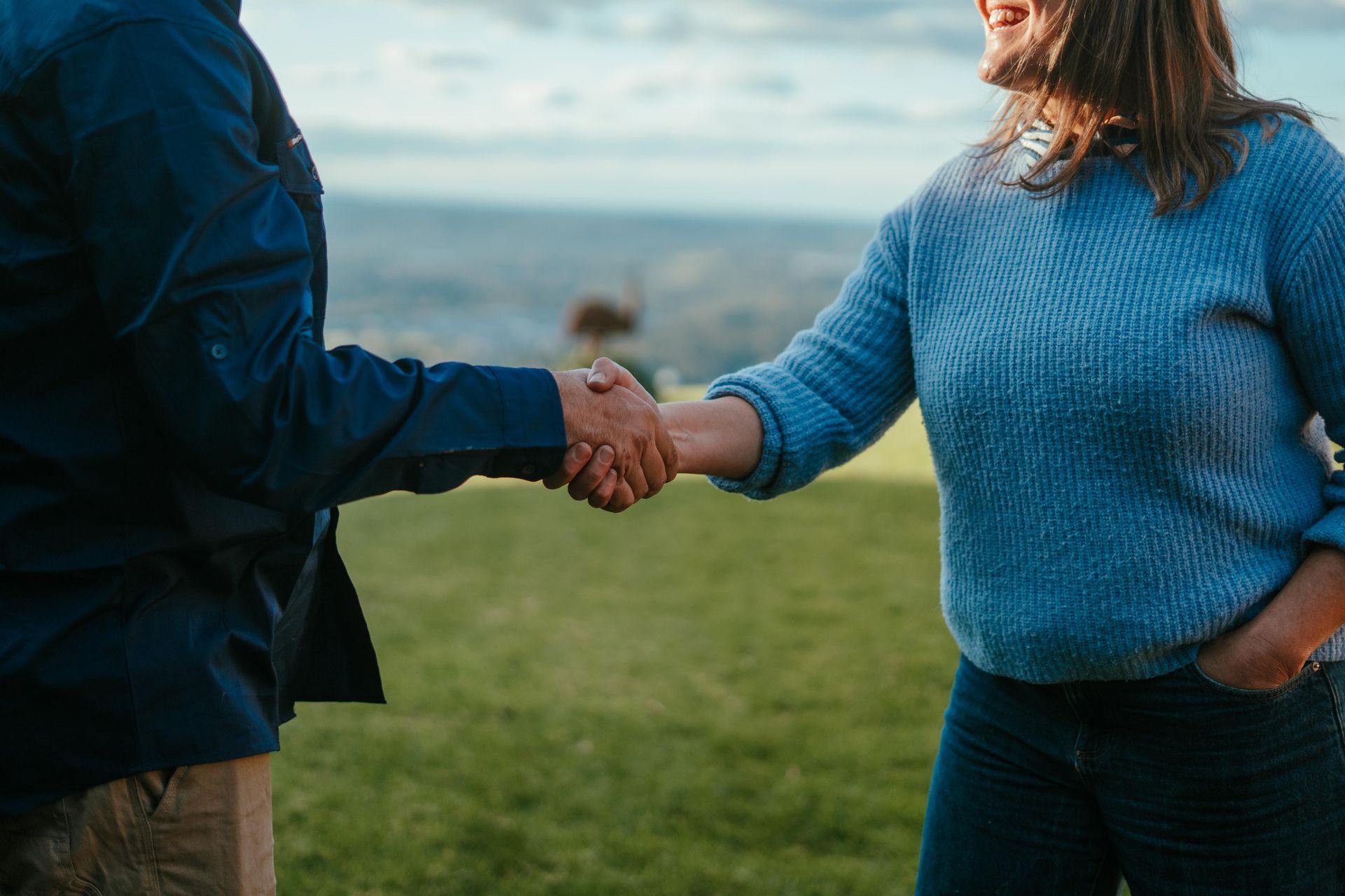 Two people in blue jackets shaking hands outdoors on a grassy field. — The Plumbing & Drainage Co. in Mittagong, NSW