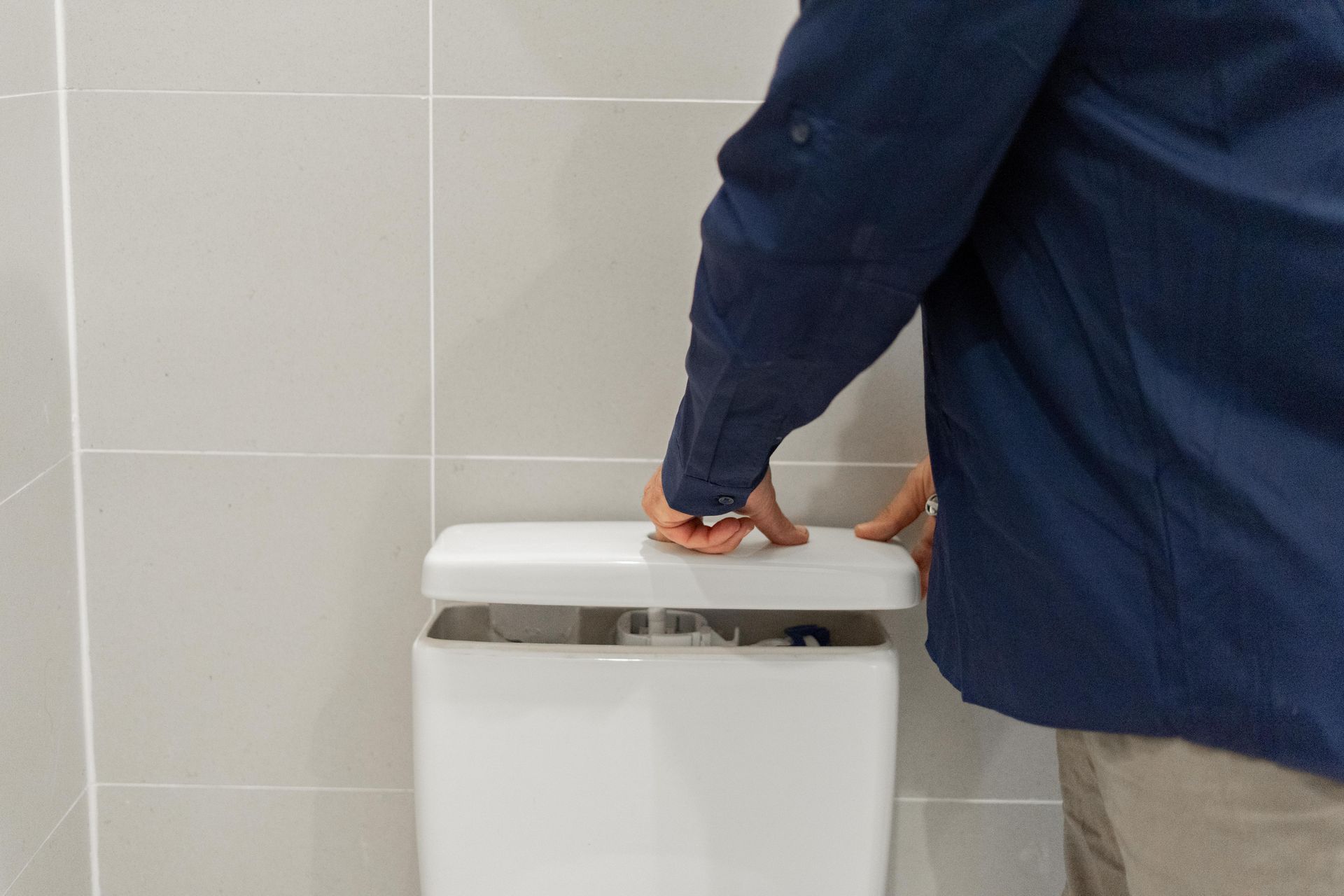 Person in a blue jacket pressing a white toilet flush in a tiled restroom. — The Plumbing & Drainage Co. in Southern Highlands, NSW