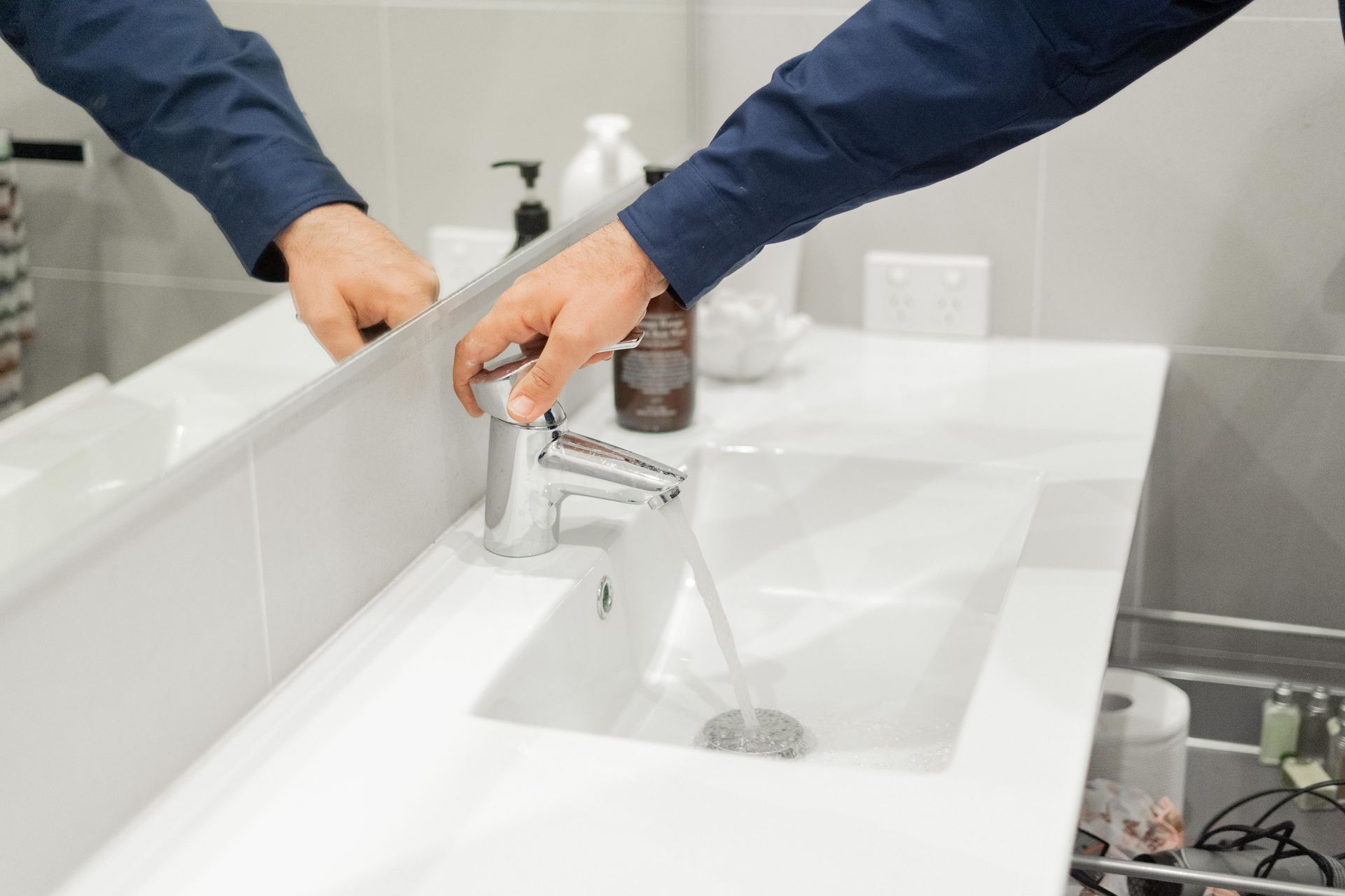 Hands washing at a white bathroom sink with running water — The Plumbing & Drainage Co. in Campbelltown, NSW