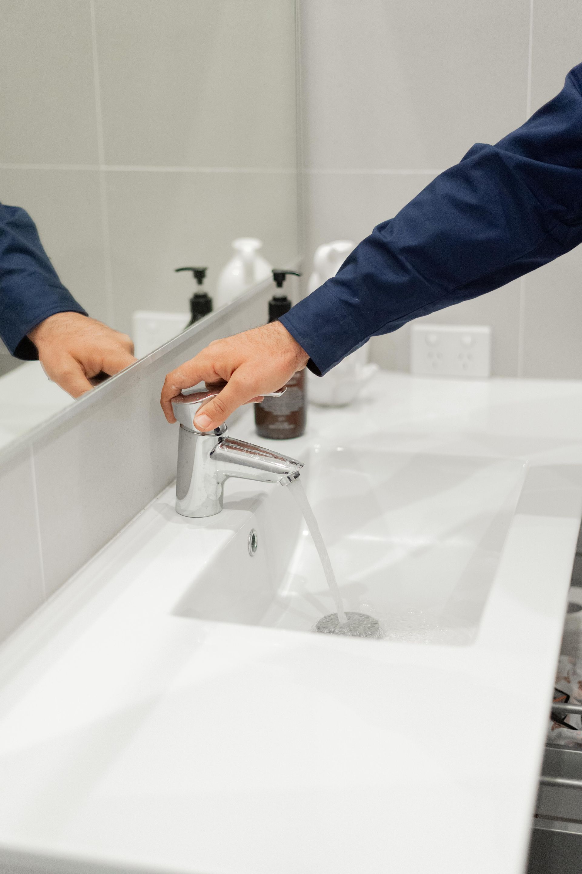 Hands washing under running water at a white sink with a chrome faucet in a restroom — The Plumbing & Drainage Co. in Shellharbour, NSW