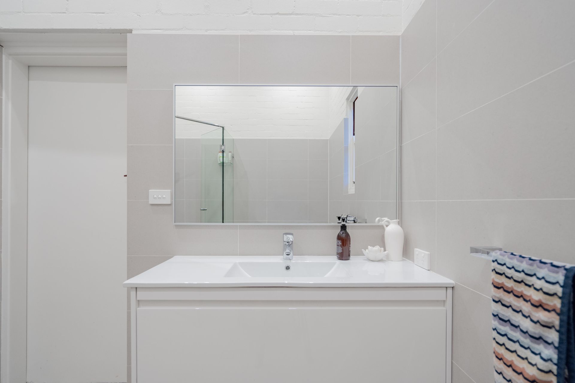 Minimalist white bathroom vanity with mirror, sink, shower, and striped towel — The Plumbing & Drainage Co. in Mittagong, NSW