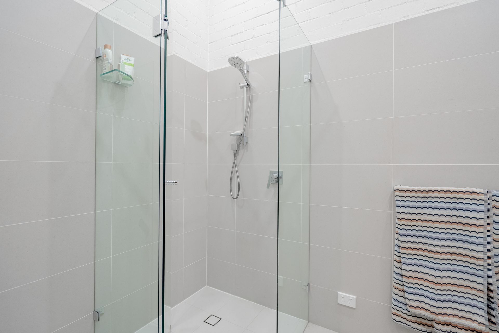 Modern tiled shower with glass enclosure and handheld showerhead in a bright bathroom — The Plumbing & Drainage Co. in Mittagong, NSW