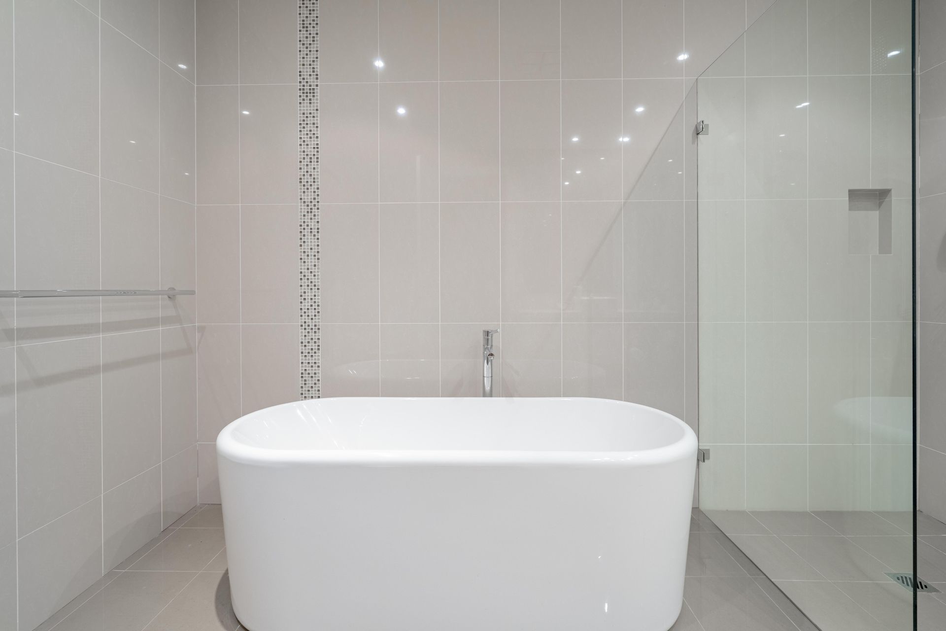 Modern white freestanding bathtub in a minimalist tiled bathroom with glass shower walls — The Plumbing & Drainage Co. in Mittagong, NSW