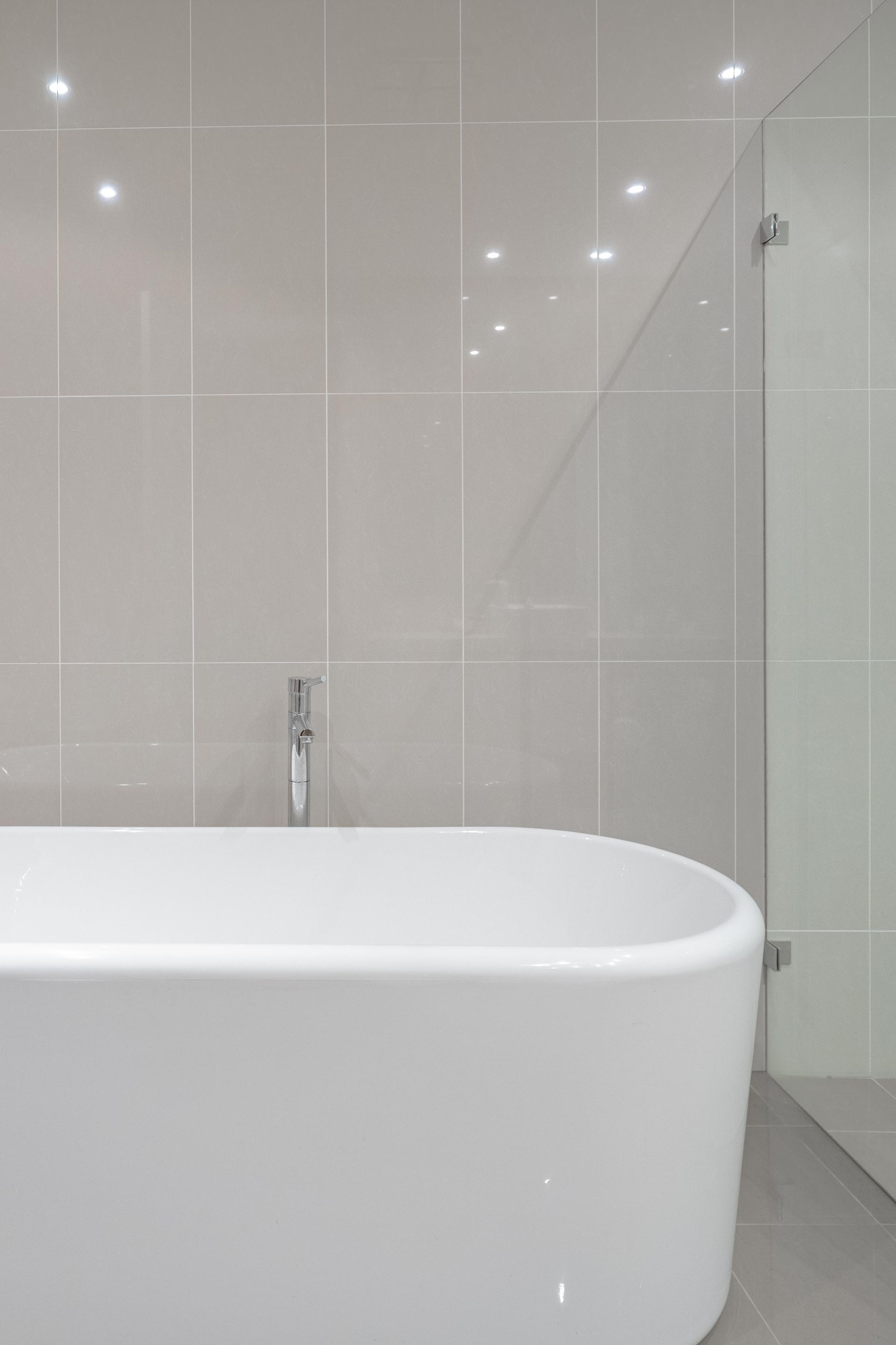 Modern bathroom with a white freestanding tub, gray tile walls, and glass shower enclosure — The Plumbing & Drainage Co. in Wollongong, NSW