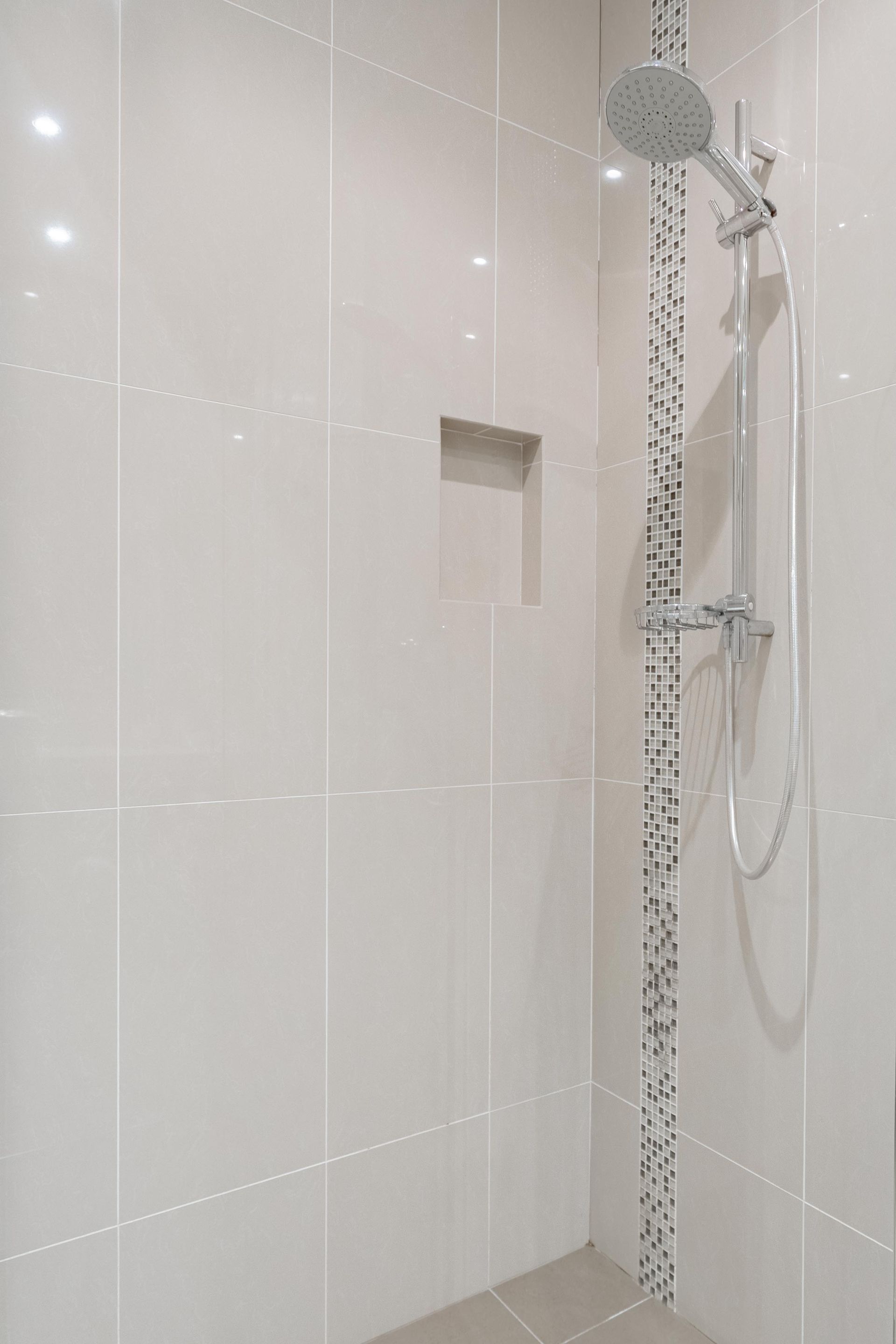 Modern white-tiled shower with a rain showerhead, handheld shower, and built-in shelf. — The Plumbing & Drainage Co. in Southern Highlands, NSW