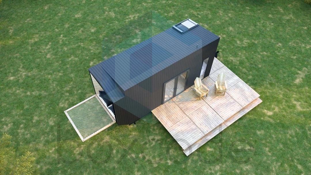 Black, modern tiny house on a grassy area with wooden decks and a sun roof.