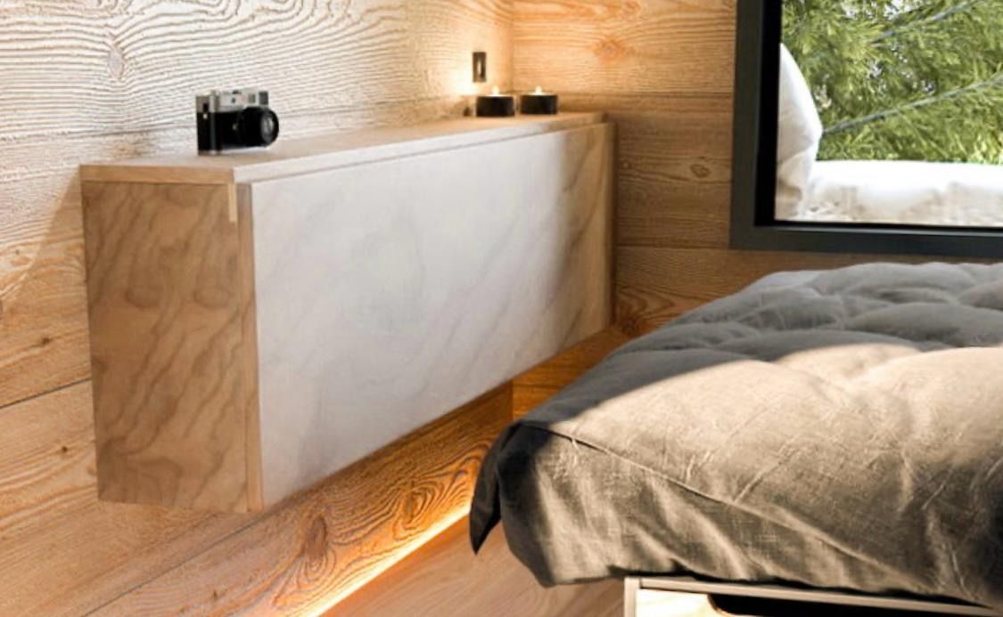 Floating wooden shelf with a camera and candles above a bed in a wood-paneled room.