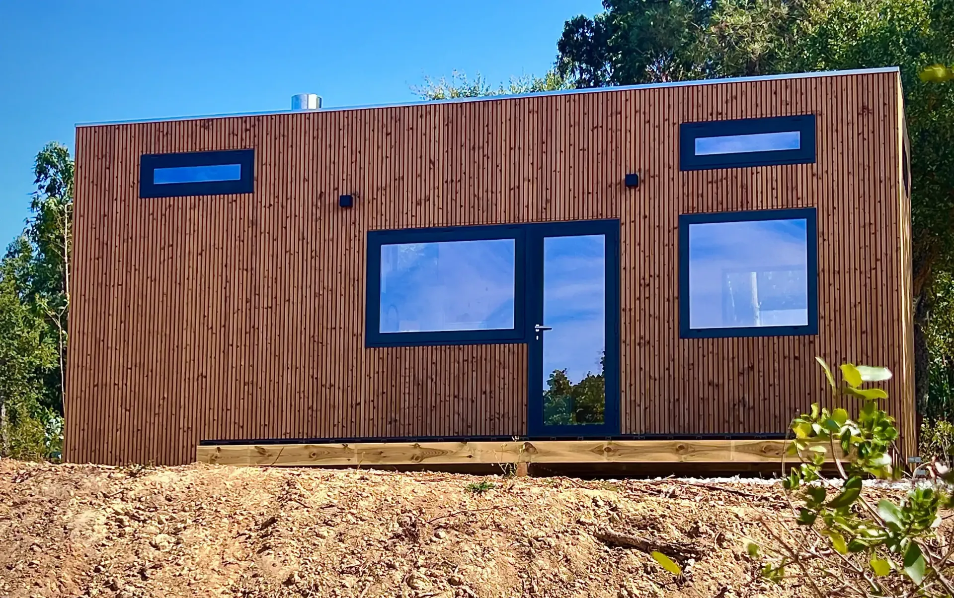 Tiny, modern cabin with brown siding, dark window frames, and glass door on a wooden deck.