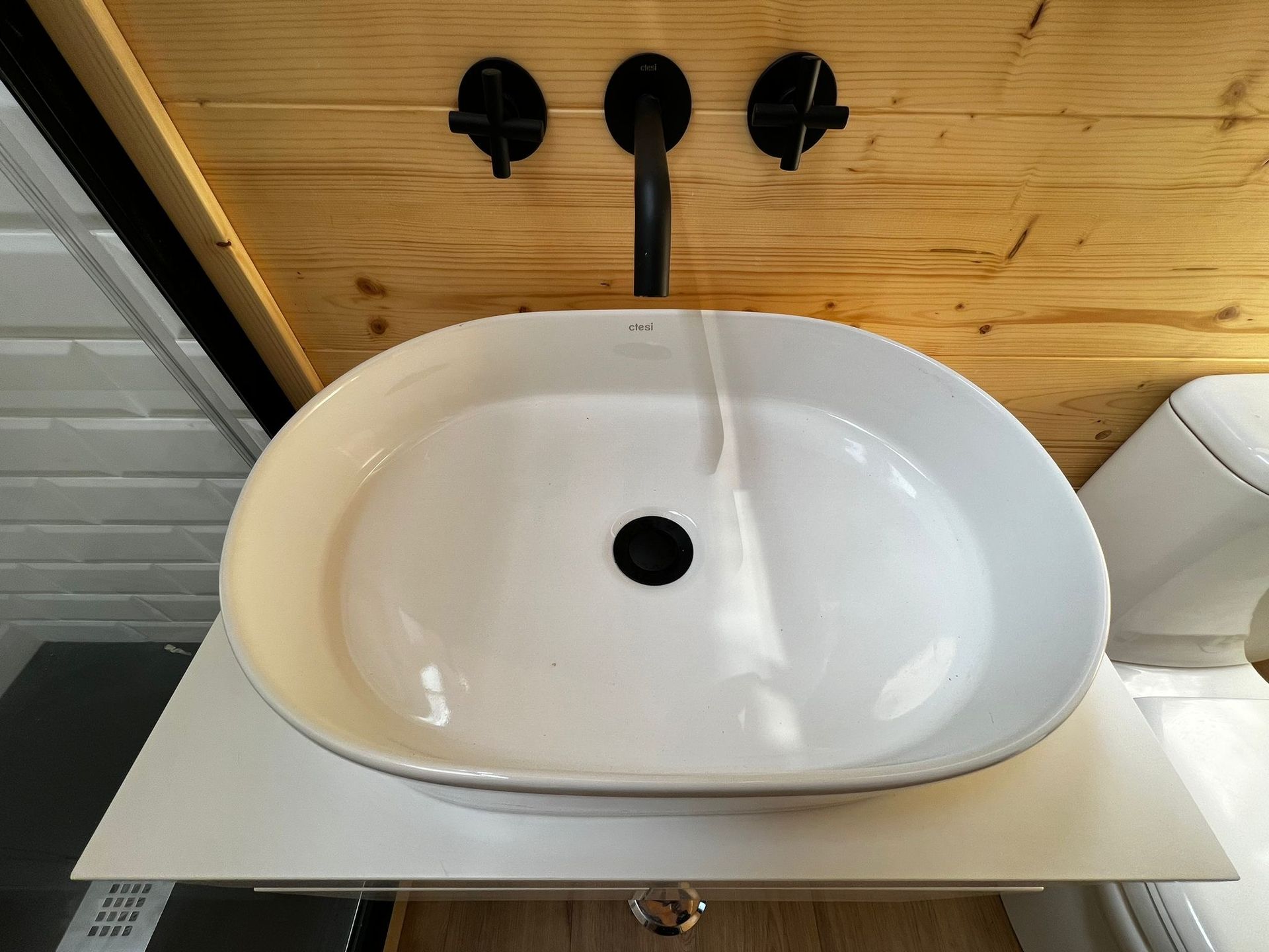 White oval bathroom sink with black faucet on a wooden wall.