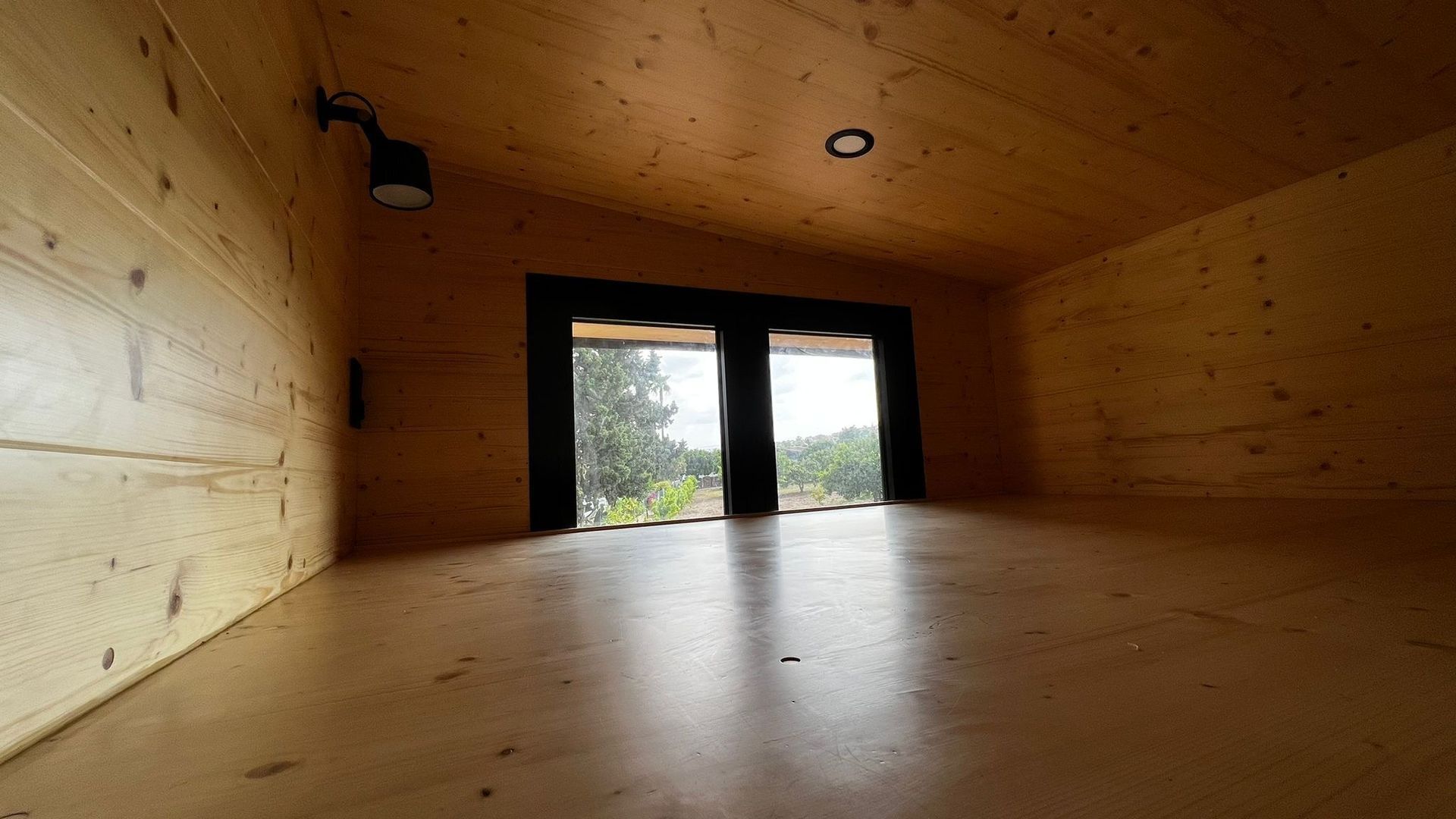 Wooden interior with angled ceiling, small window, and open space.