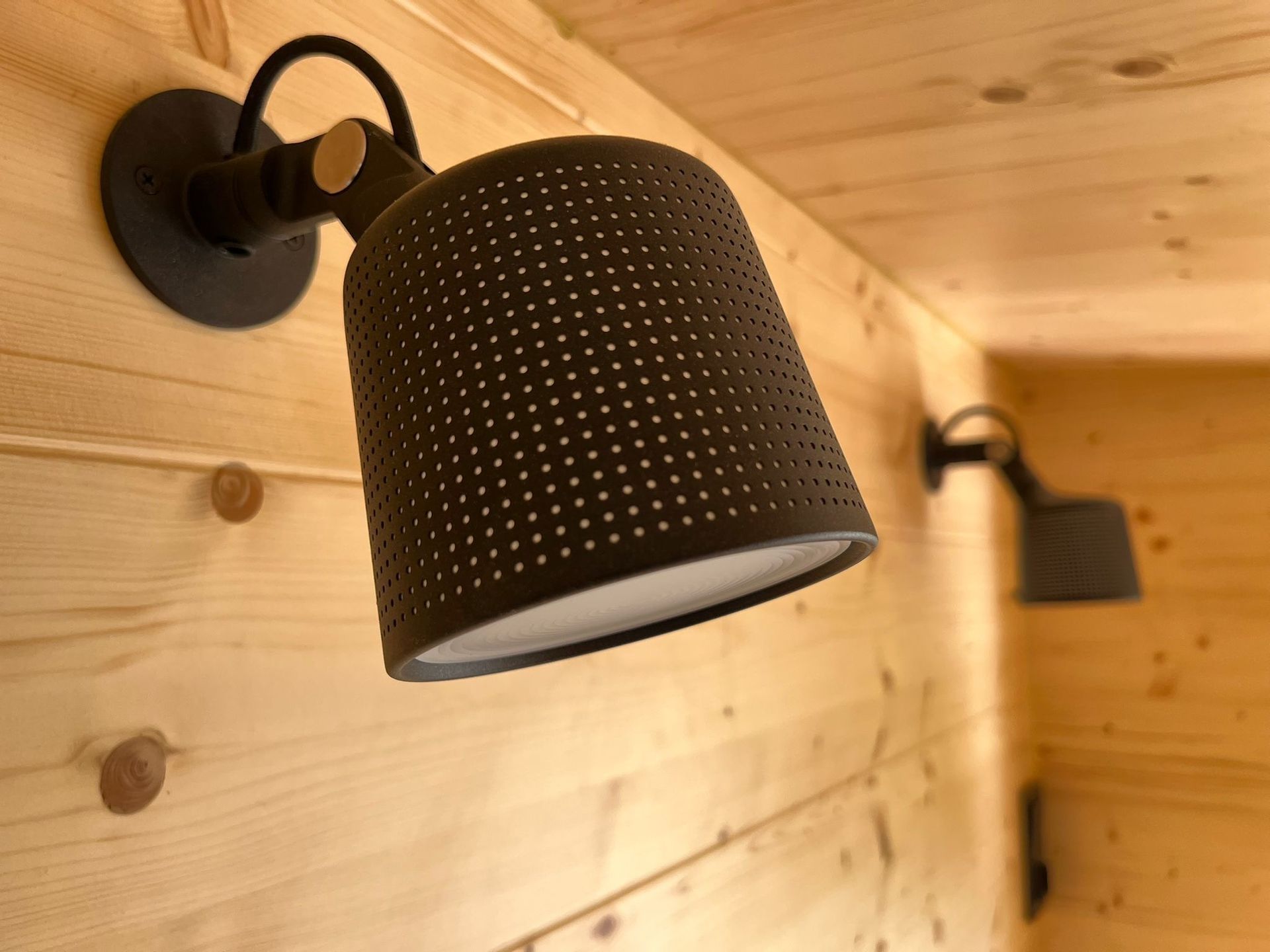 Two black, perforated lamps mounted on a light wood wall.