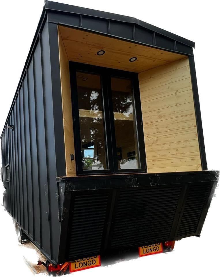 Black tiny home with a wooden porch and large window.