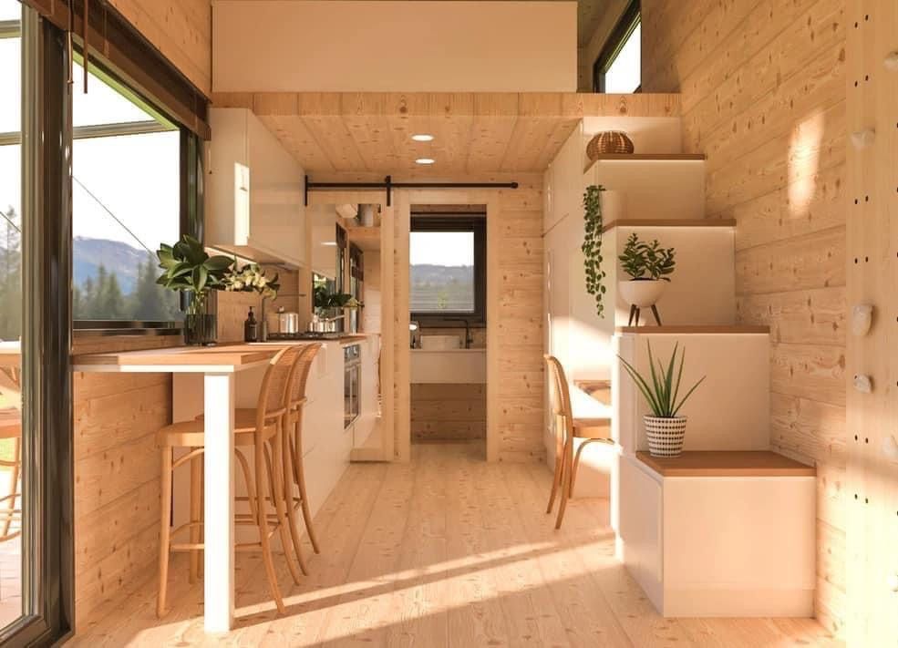 Interior of a tiny home with wooden walls, kitchen, stairs to loft, and bar seating.