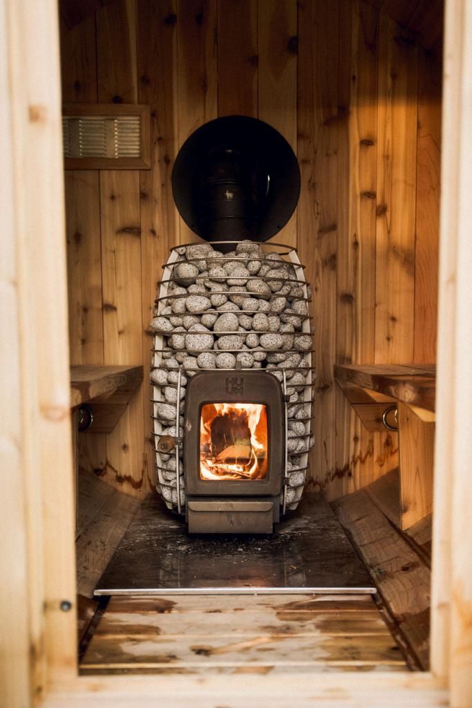 Sauna interior with a wood-burning stove made of stone and a large black sphere on top, wooden benches.