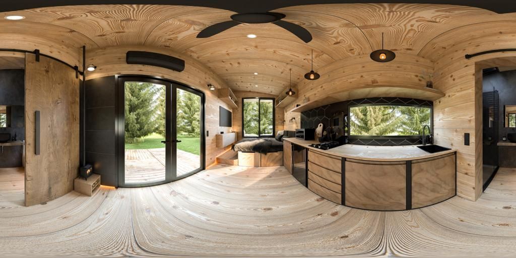 Interior of a tiny home, featuring wooden walls, a curved kitchen, and large windows with an outside view.