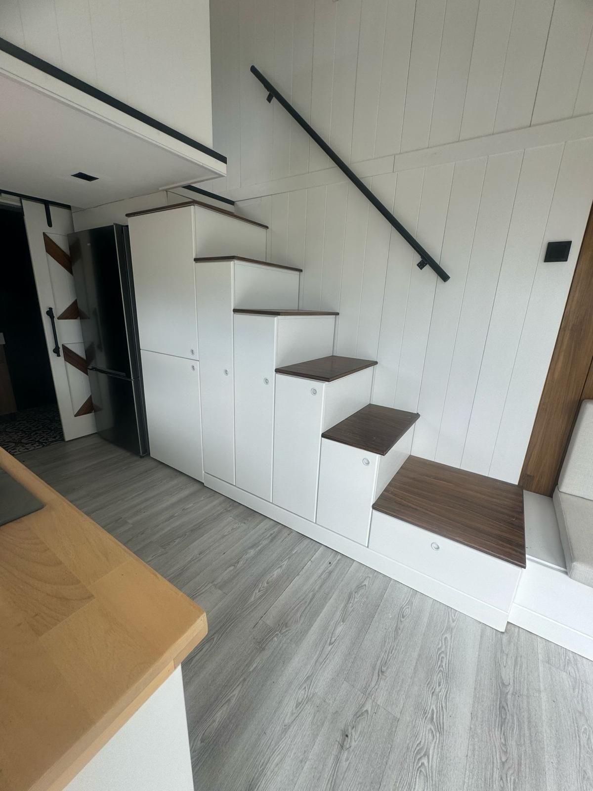 White cabinet stairs with dark wood steps and a black railing in a modern interior.