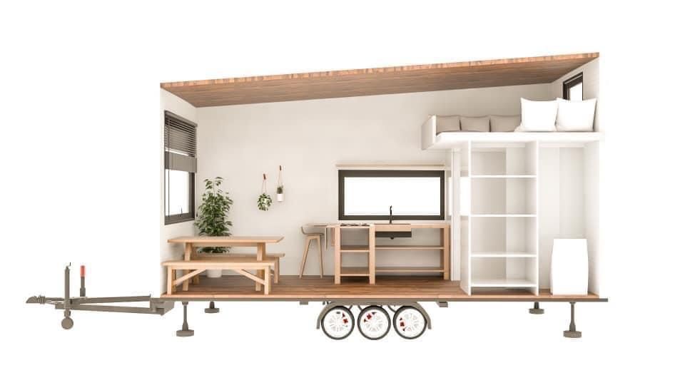 Cutaway view of a tiny home on wheels, with a dining area, kitchen, and loft bedroom.