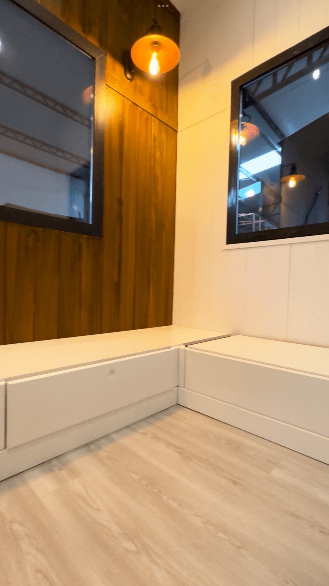 Corner seating with windows and wood paneling, lit by a hanging bulb; light wood flooring.