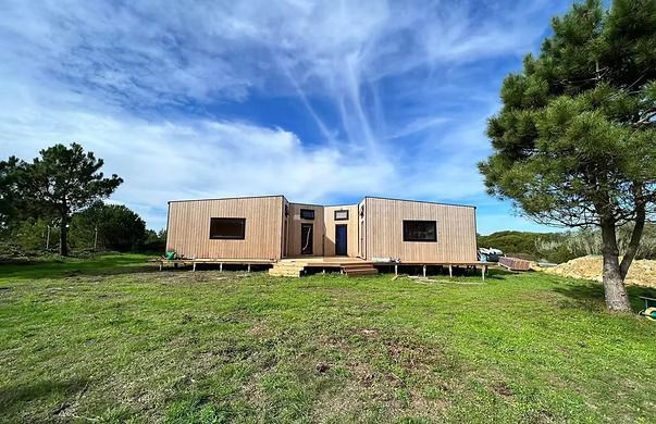 Wooden cabin in a grassy field under a bright blue sky with scattered clouds.
