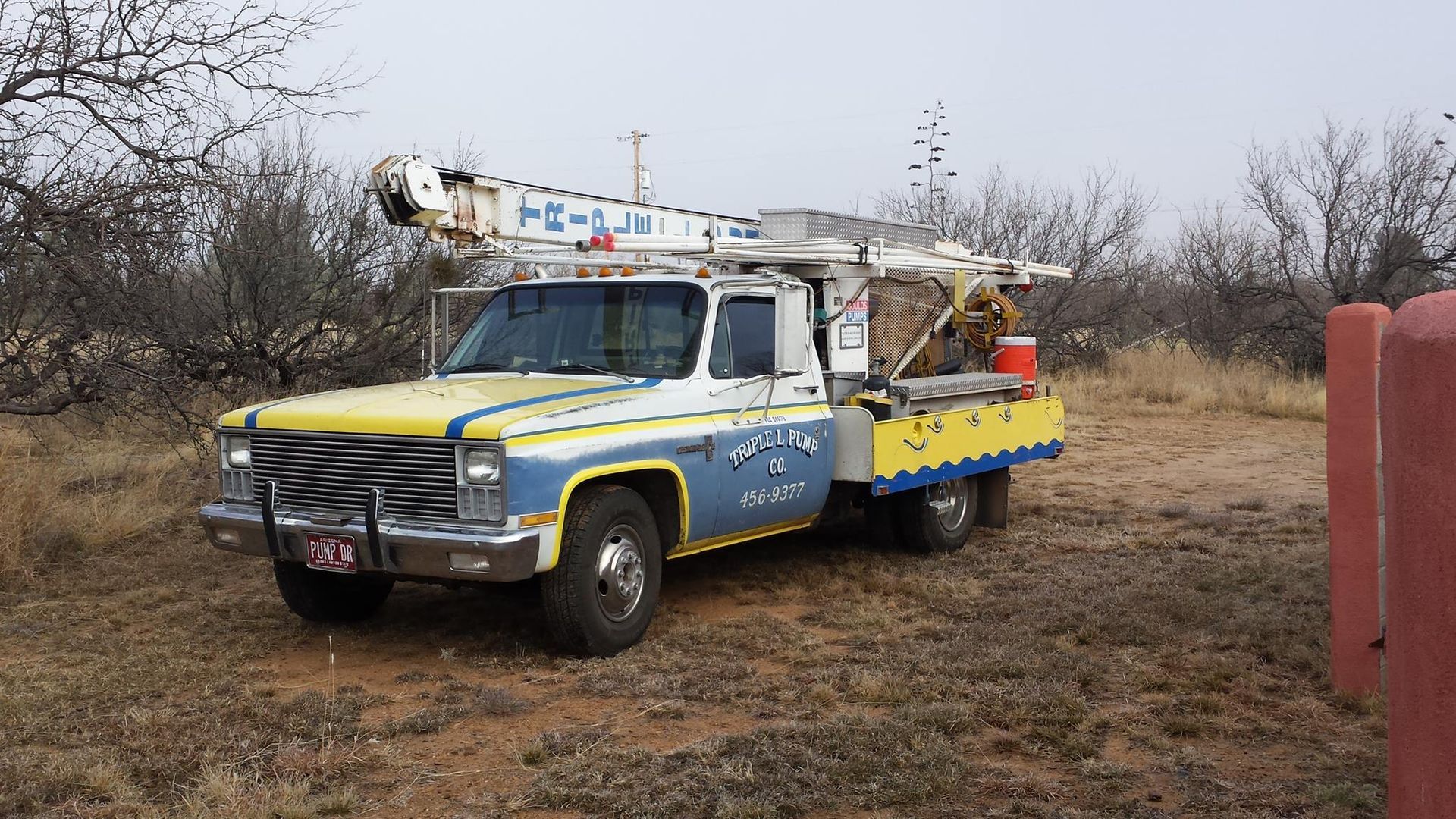 a yellow and blue truck with a crane on top of it is parked in a field .