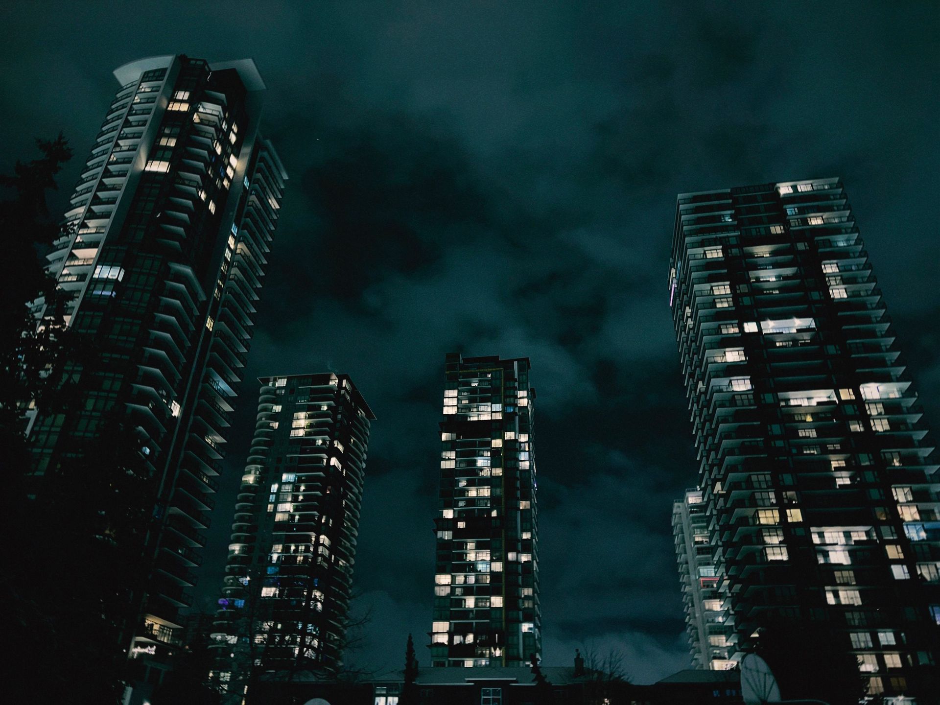 Dark city skyline with tall lit apartment towers under a cloudy night sky