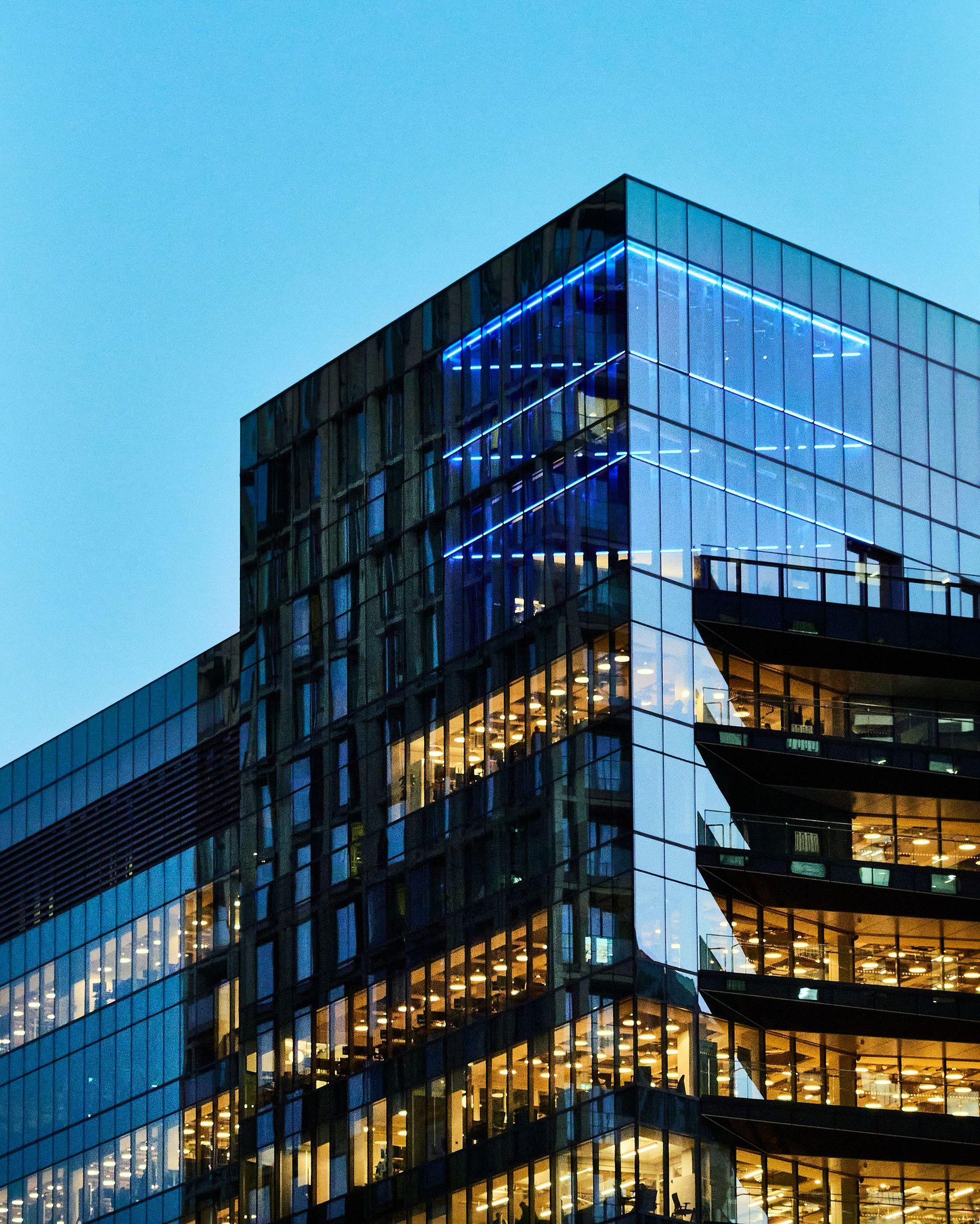 Glass office building glowing blue at dusk against a clear sky