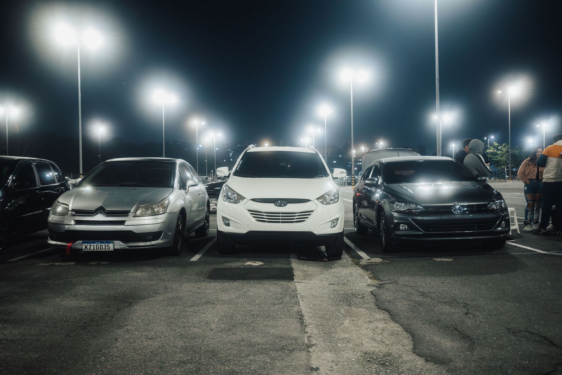 Three parked cars under bright lights in a night parking lot