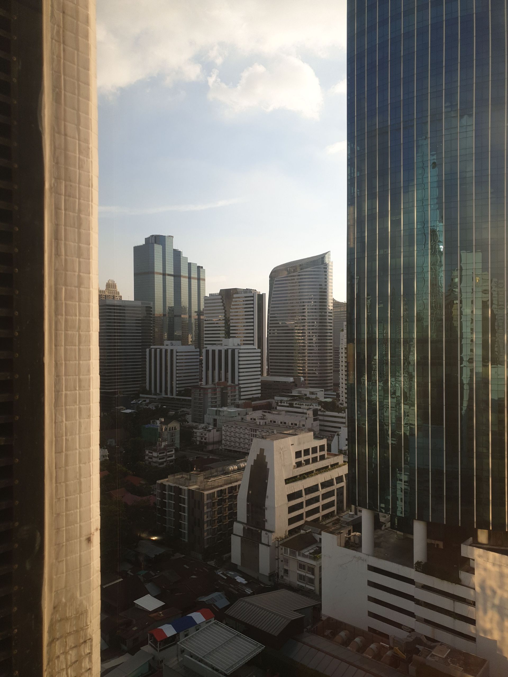 City skyline viewed through a window at sunset, with tall glass buildings and warm light.