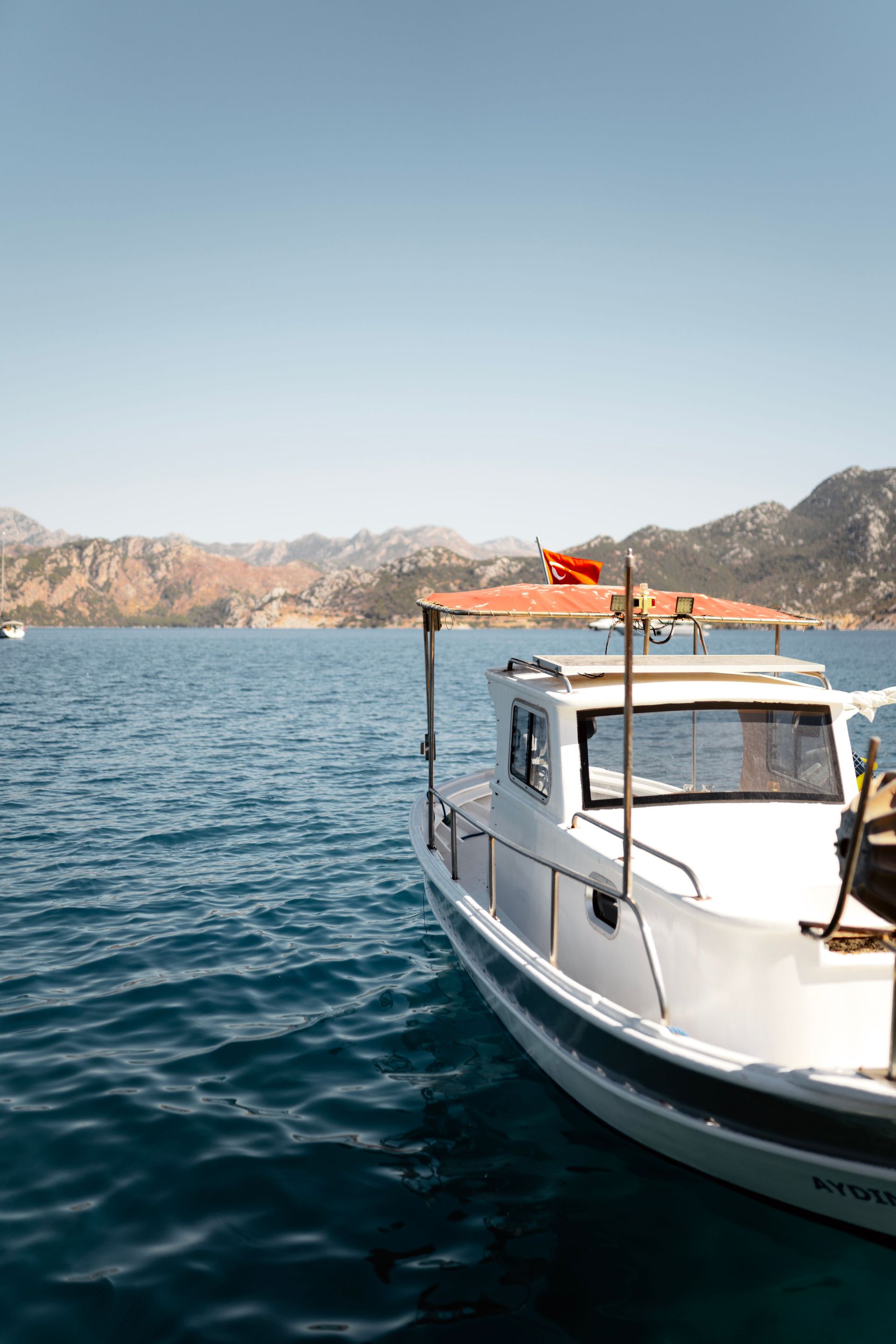 Small white boat on blue water near rocky mountains under a clear sky