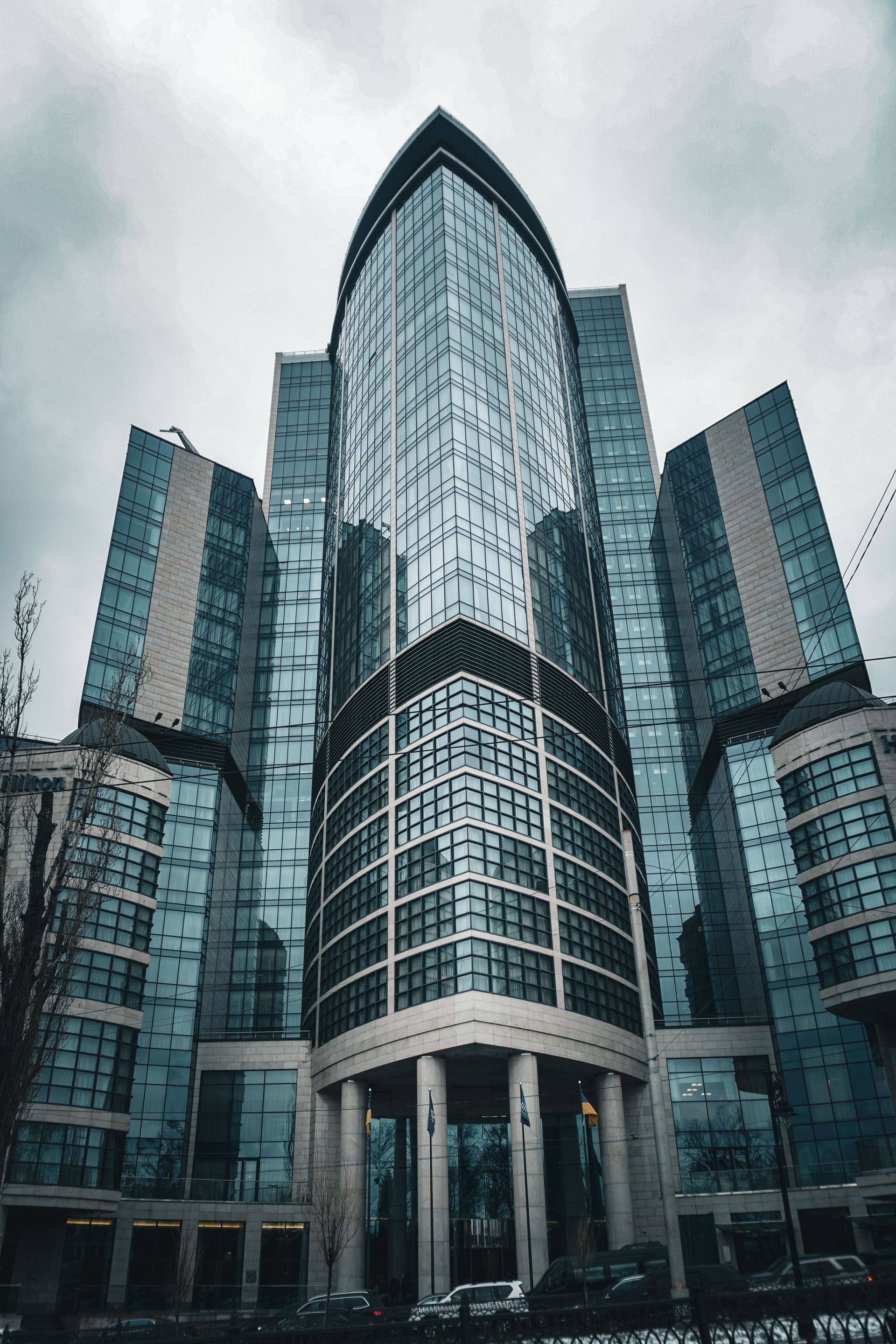 Glass office tower with a pointed roof and curved facade against a cloudy sky