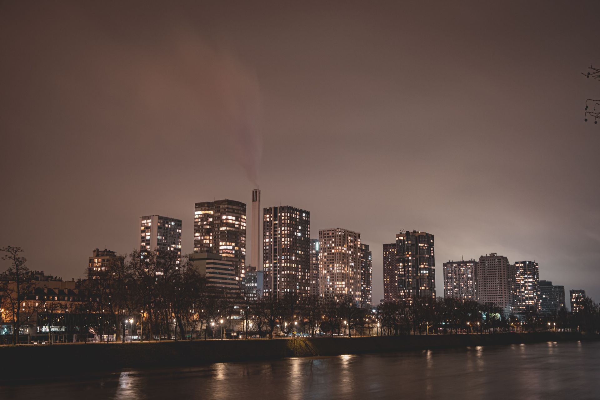 Nighttime city skyline with illuminated high-rises reflected on calm water under a cloudy sky
