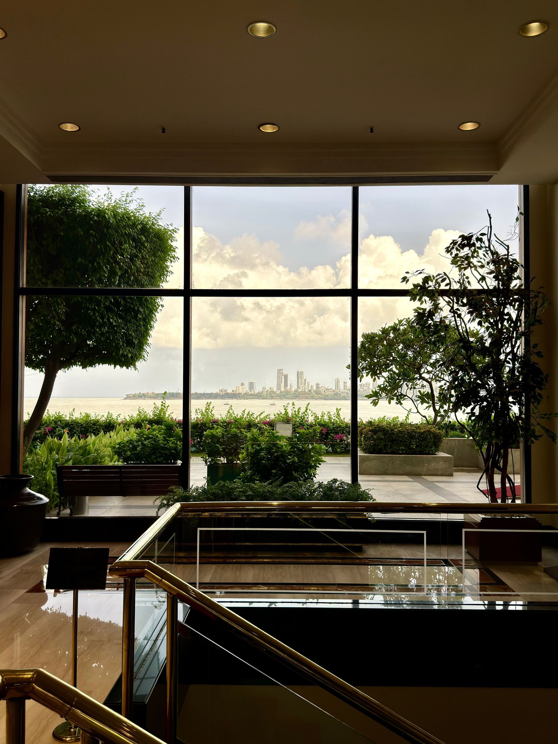 Elegant living room with floor-to-ceiling windows overlooking a lush garden and city skyline at sunset