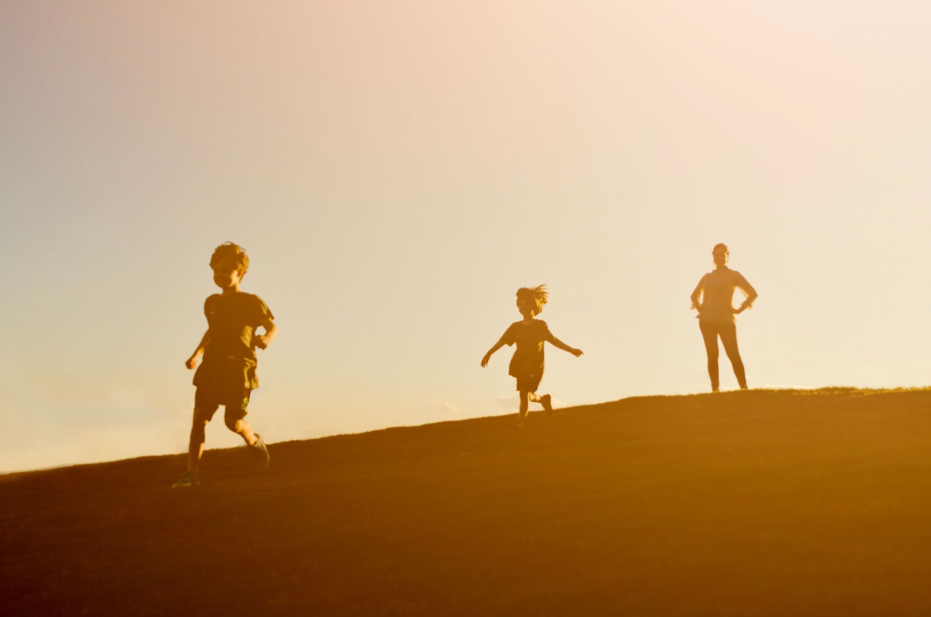 Three children running and standing on a sunlit hill at sunset, silhouetted against a golden sky
