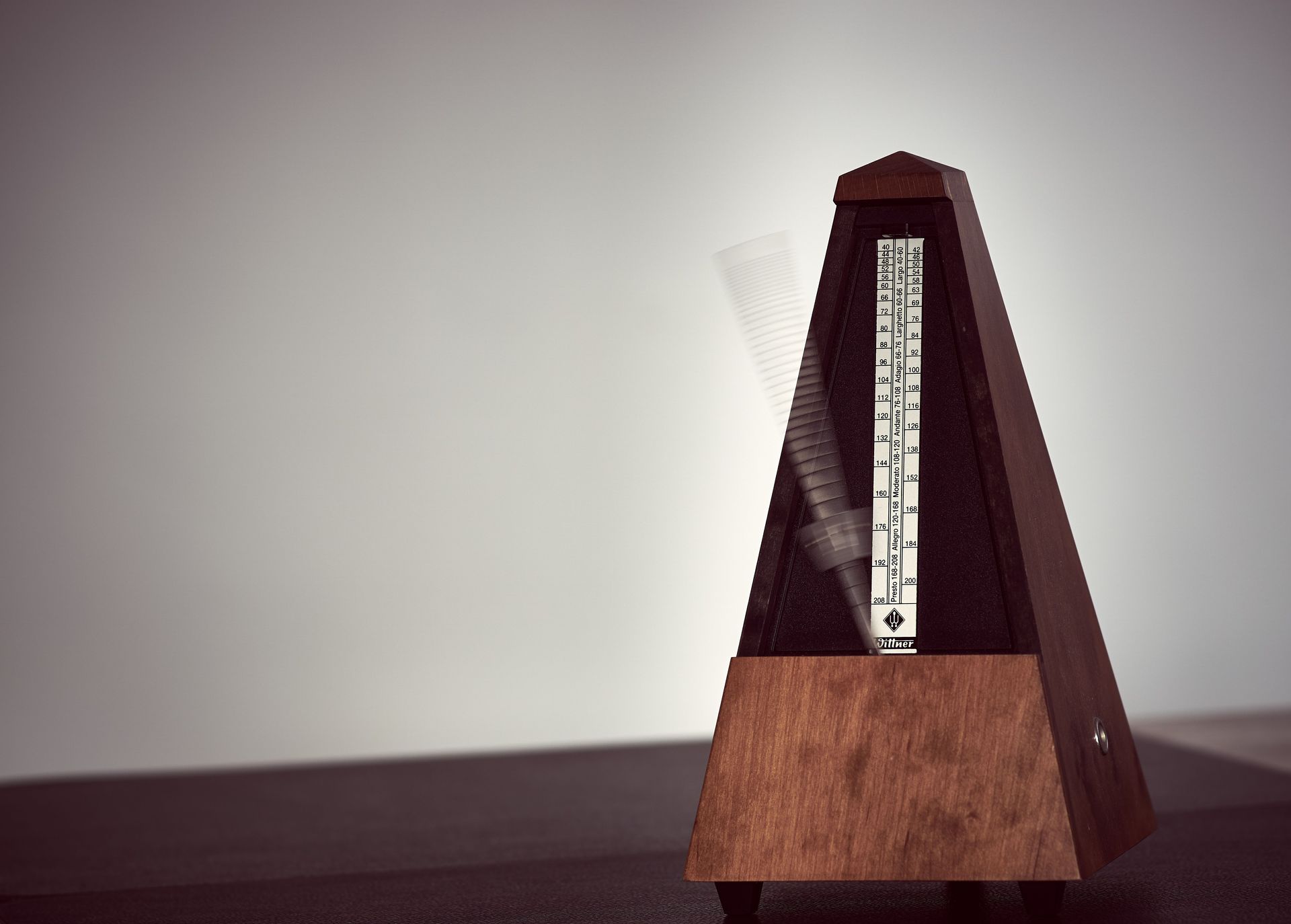 Wooden metronome on a dark tabletop against a plain light wall.