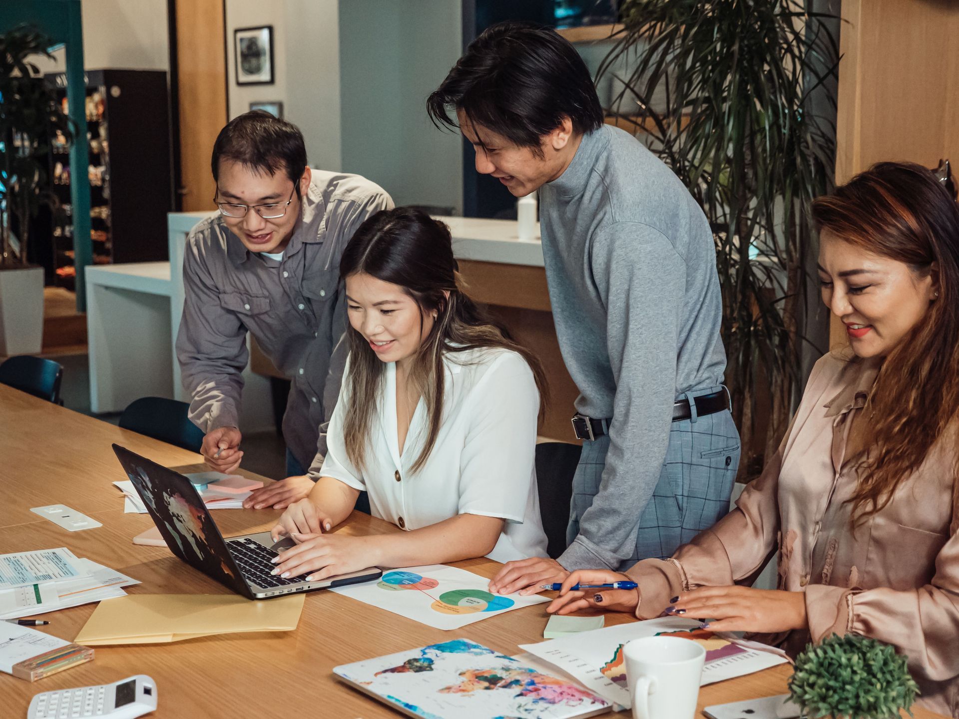 Four coworkers gather around a table, reviewing papers and a laptop in a meeting room.