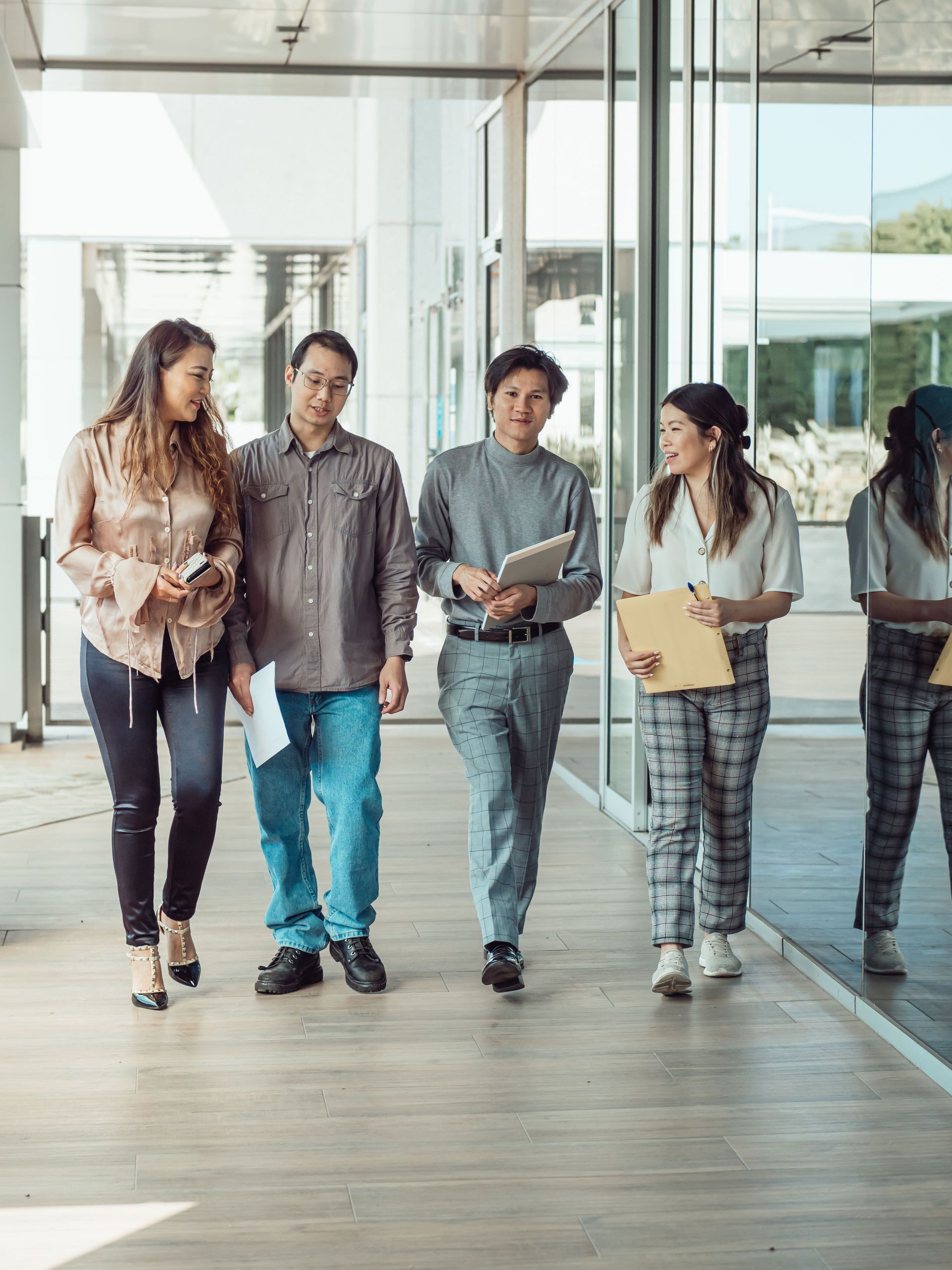 Four coworkers walking through a bright office lobby, carrying folders and a laptop.