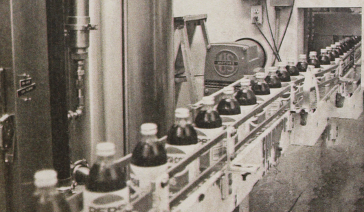 Black and white photo of vintage Pepsi bottles going through a factory line.