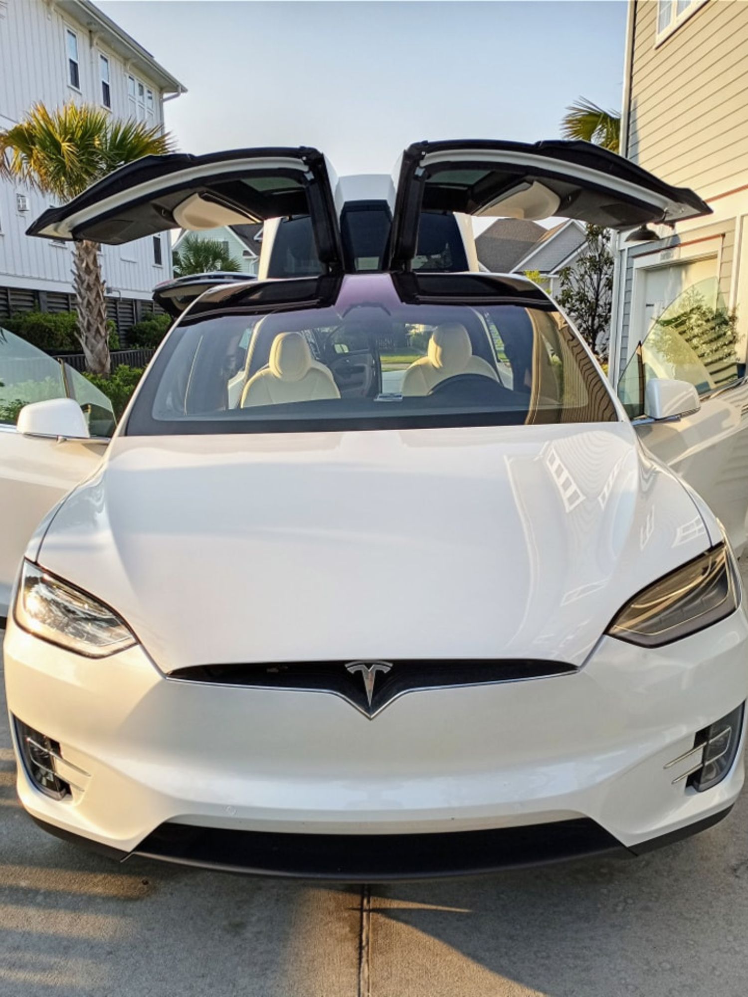 A white tesla model x with its doors open is parked in front of a house.