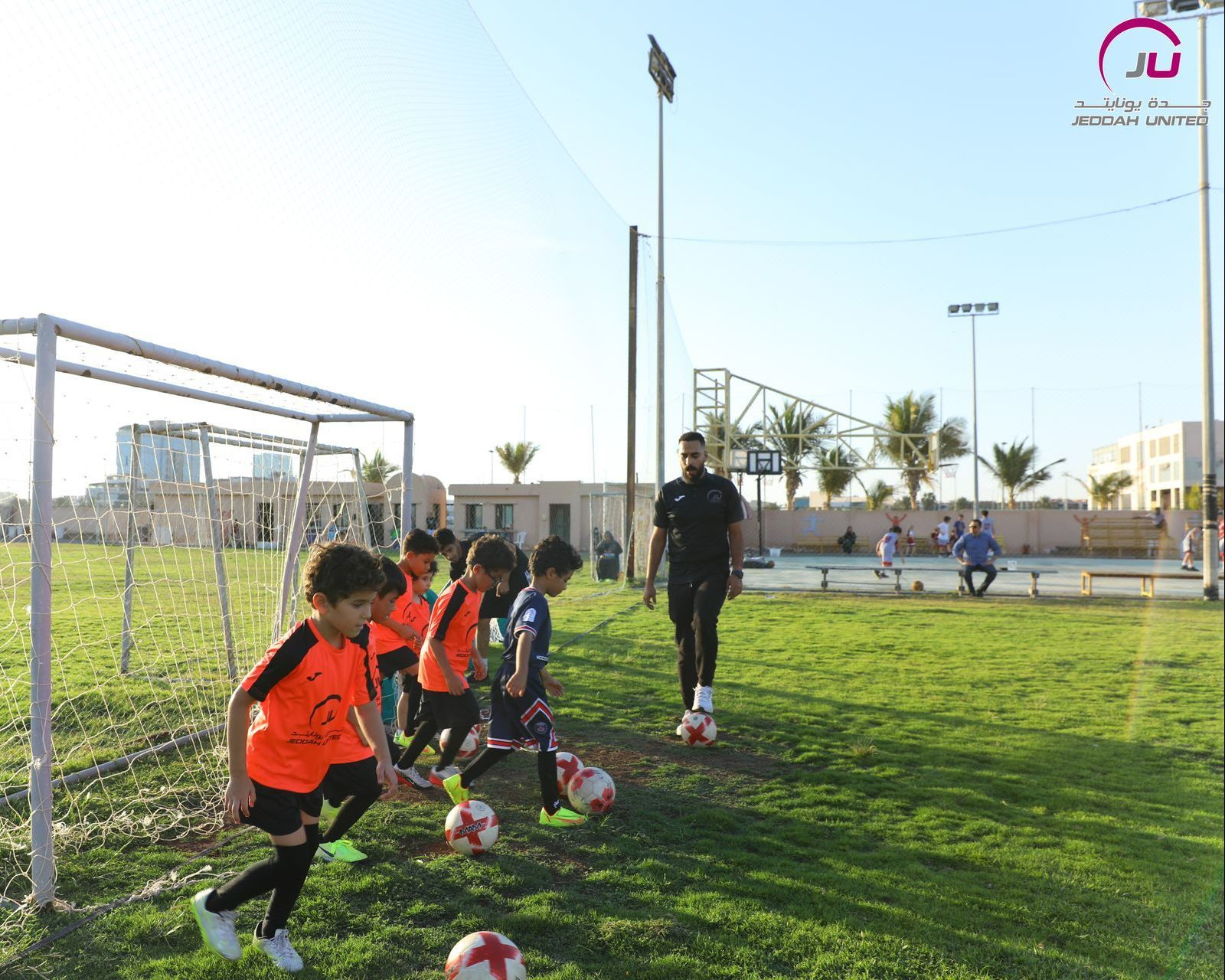 a coach teaching young boys football in Jeddah United field a coach teaching young boys football