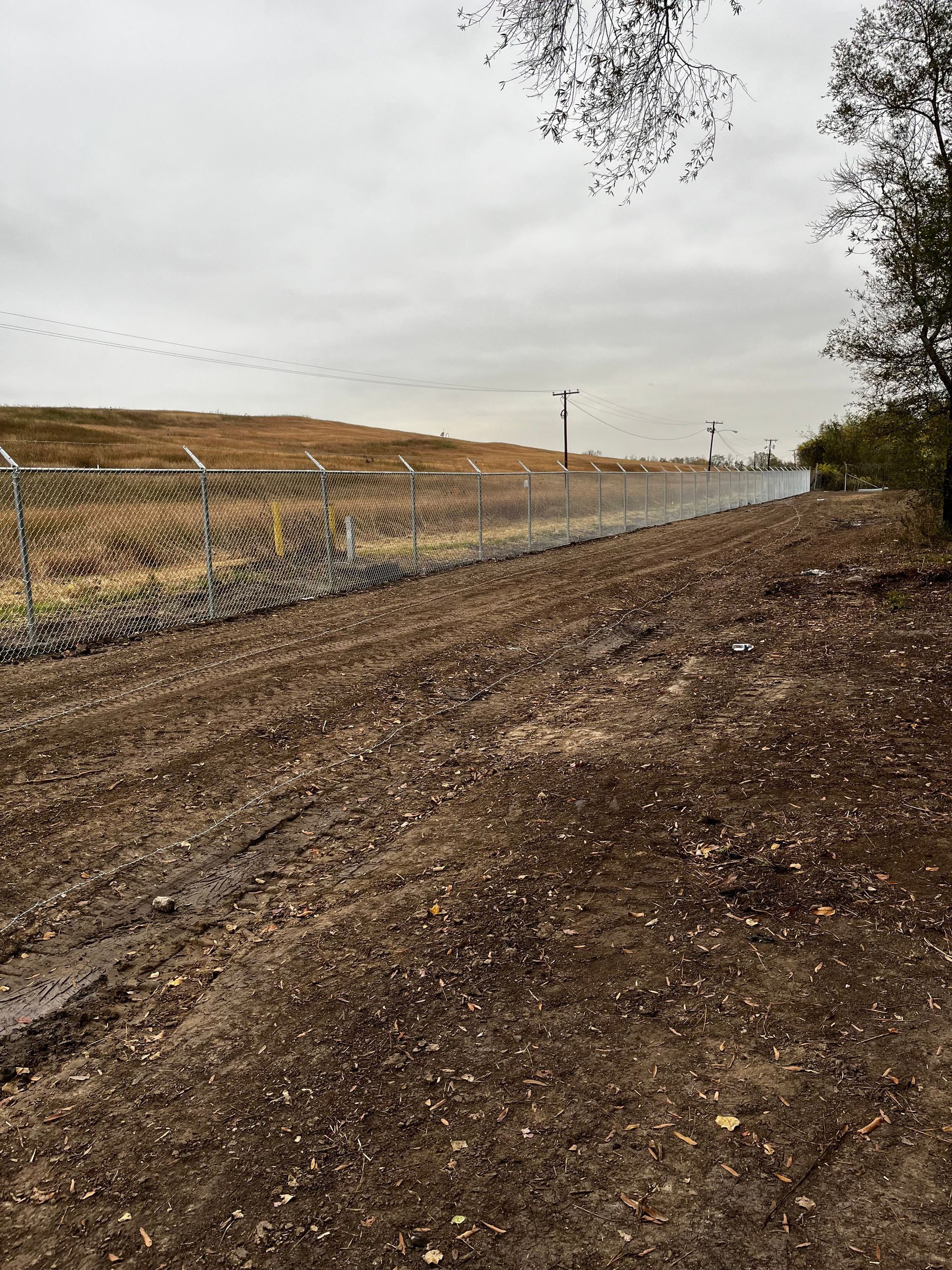 Dirt path alongside a chain-link fence, under an overcast sky.