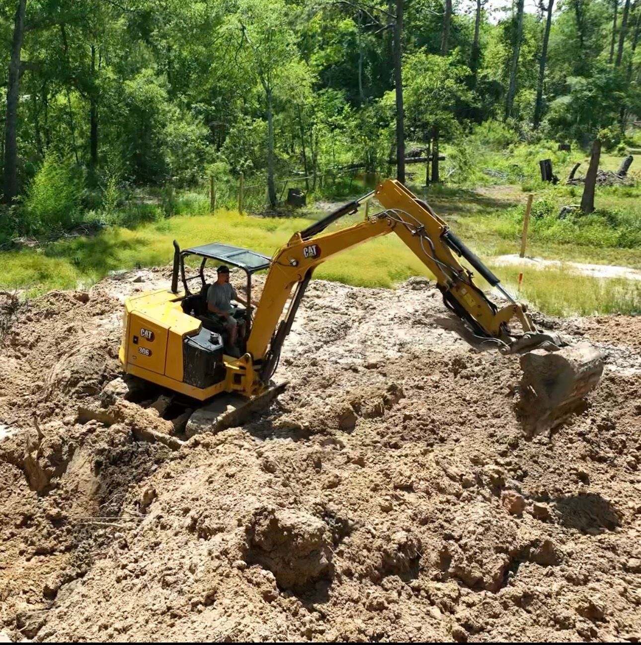 Yellow construction vehicle in a wooded area, clearing debris and dirt.