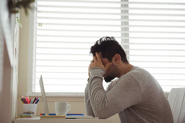 een man zit aan een bureau met zijn hoofd in zijn handen.