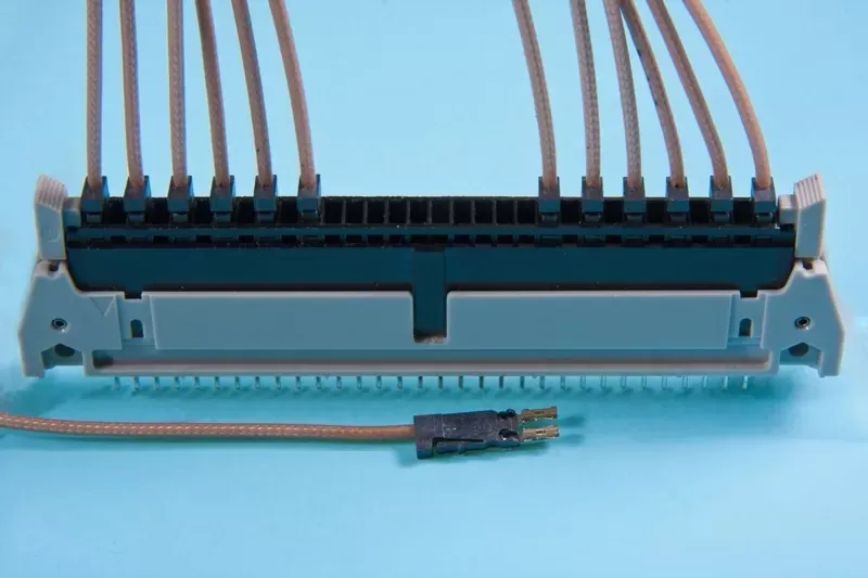 A black terminal block with tan wires connected to the top and one loose wire with a two-pin connector in the foreground.