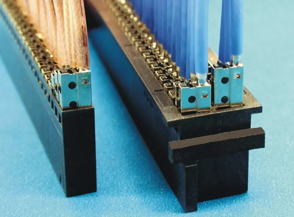 Two black terminal blocks with metal connection points, one with wires attached, against a light blue background.