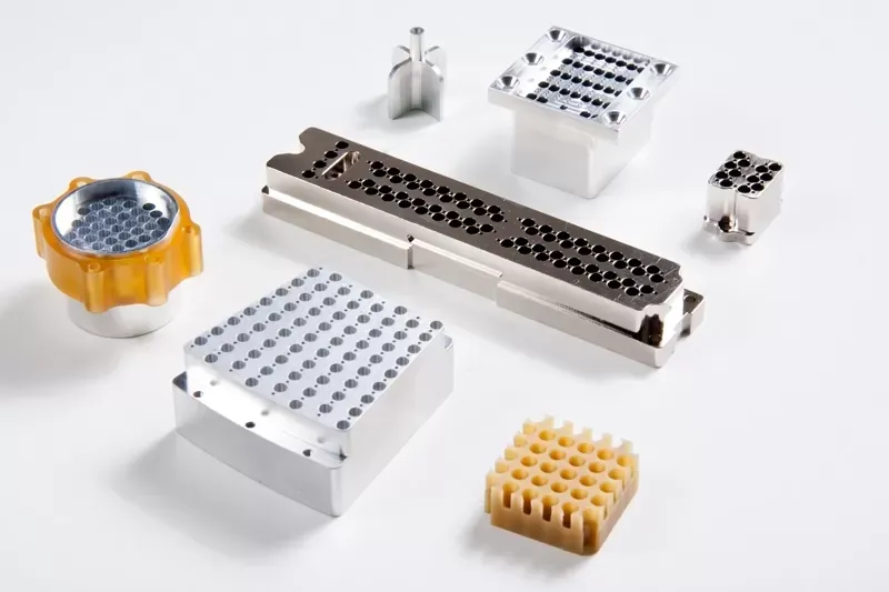 A group of industrial precision metal and polymer components with grid-like hole patterns, set against a white background.