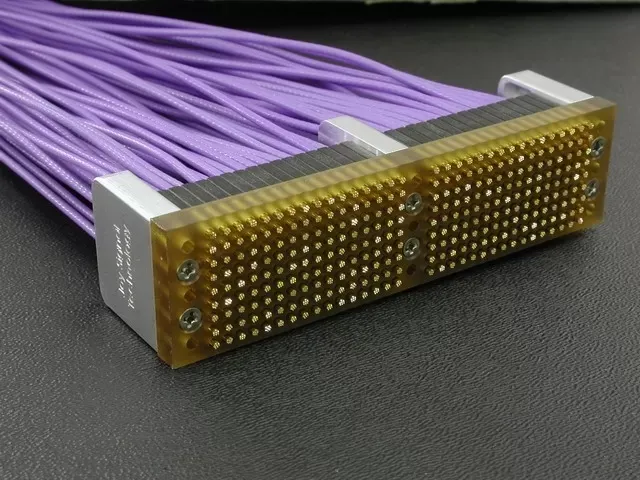 A multi-pin connector block with many lavender wires attached, set against a dark background.