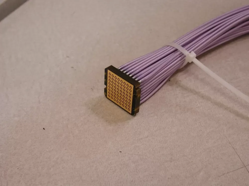 A bundle of light-purple electrical wires ending in a square-shaped, gold-plated multi-pin connector on a gray surface.