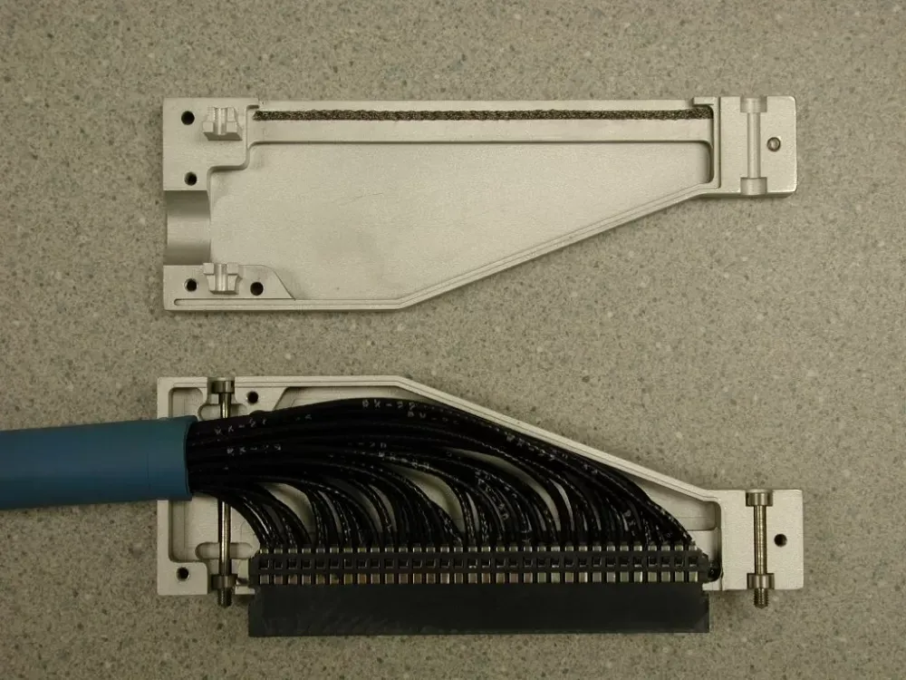 An open metal connector housing showing a multi-strand black cable wired into a long black electrical terminal block.